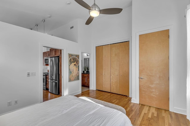 bedroom with ensuite bathroom, high vaulted ceiling, light wood-type flooring, stainless steel refrigerator, and ceiling fan