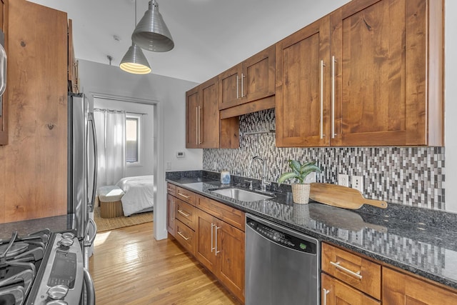 kitchen with pendant lighting, sink, dark stone counters, light hardwood / wood-style floors, and stainless steel appliances