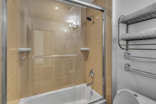 bathroom featuring toilet and bath / shower combo with glass door