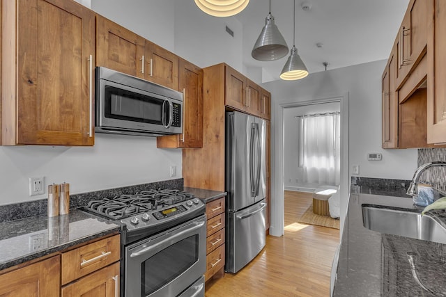 kitchen with sink, appliances with stainless steel finishes, hanging light fixtures, light hardwood / wood-style floors, and dark stone counters