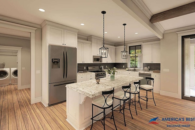 kitchen with a breakfast bar area, decorative light fixtures, appliances with stainless steel finishes, a kitchen island, and independent washer and dryer