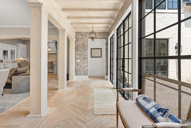 corridor featuring plenty of natural light, beam ceiling, decorative columns, and a notable chandelier