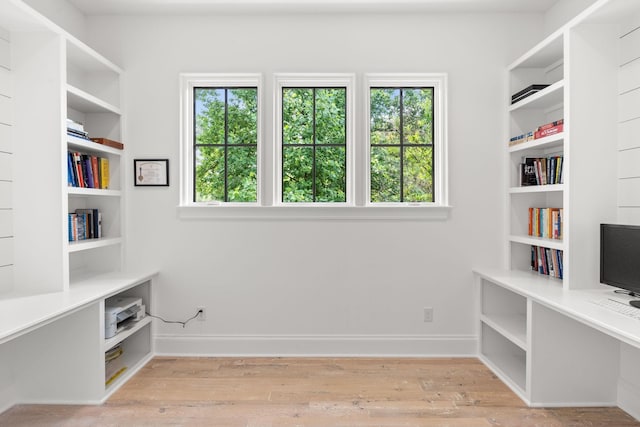 unfurnished office with built in desk, a healthy amount of sunlight, and light wood-type flooring