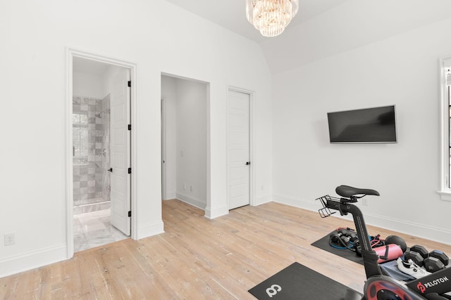 workout area featuring a notable chandelier, lofted ceiling, and light wood-type flooring