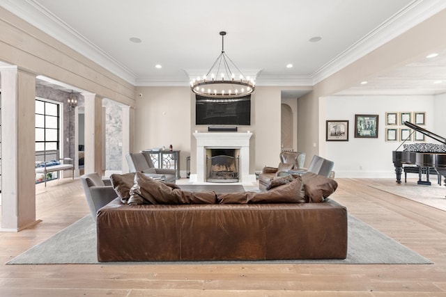 living room featuring ornate columns, ornamental molding, a notable chandelier, and light hardwood / wood-style floors