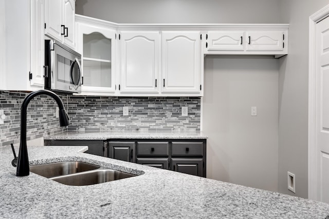 kitchen featuring tasteful backsplash, light stone countertops, sink, and white cabinets