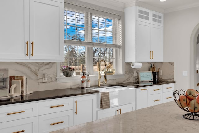 bar featuring white cabinetry, sink, backsplash, dark stone counters, and ornamental molding