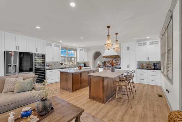 kitchen with pendant lighting, white cabinetry, a center island, stainless steel refrigerator with ice dispenser, and light hardwood / wood-style flooring