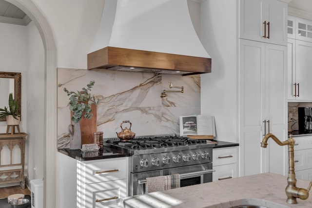 kitchen featuring sink, high end range, dark stone countertops, custom range hood, and white cabinets