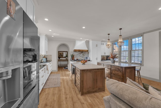 kitchen featuring white cabinetry, hanging light fixtures, custom range hood, and a kitchen island