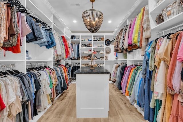 walk in closet featuring an inviting chandelier, a raised ceiling, and light hardwood / wood-style floors