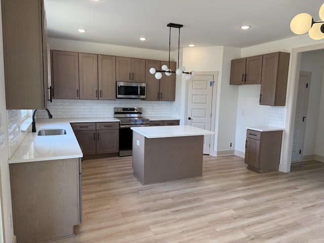 kitchen featuring sink, stainless steel appliances, light hardwood / wood-style floors, a kitchen island, and decorative light fixtures