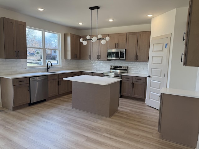 kitchen with sink, appliances with stainless steel finishes, hanging light fixtures, a center island, and light hardwood / wood-style floors