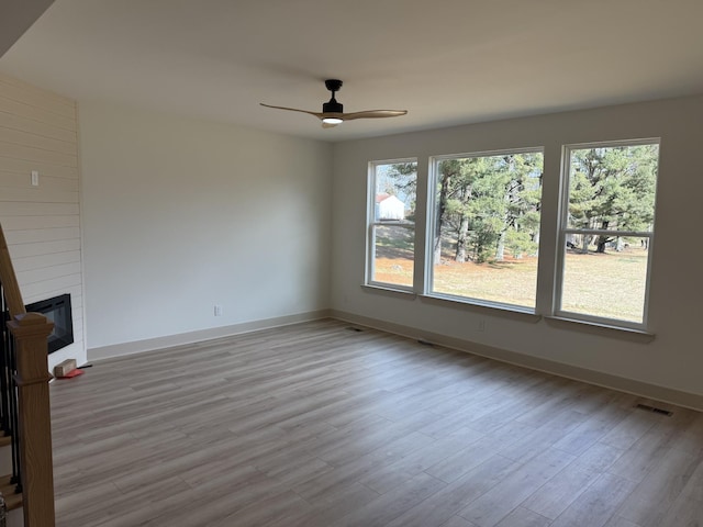 empty room with ceiling fan, plenty of natural light, a fireplace, and light hardwood / wood-style flooring