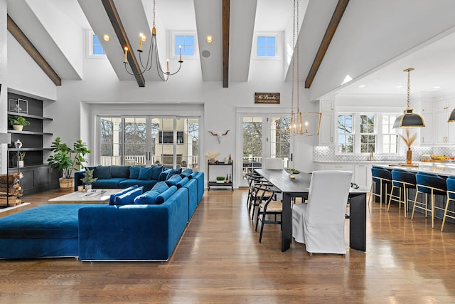 living room with beamed ceiling, wood-type flooring, a towering ceiling, and an inviting chandelier