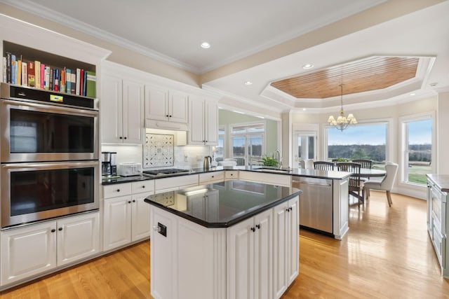 kitchen with stainless steel appliances, a tray ceiling, a kitchen island, and white cabinets