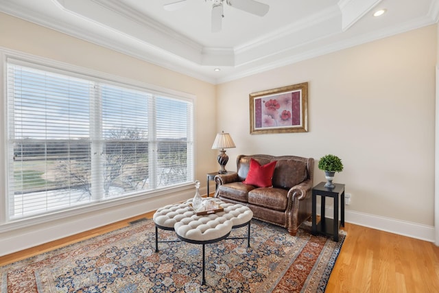 living room featuring crown molding, hardwood / wood-style flooring, a raised ceiling, and ceiling fan