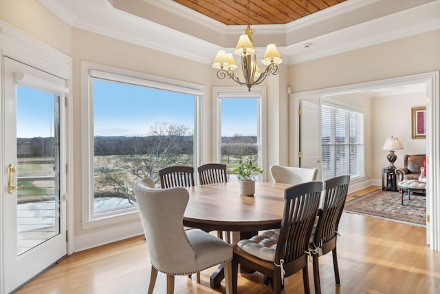 dining space with light wood-style floors, a tray ceiling, crown molding, and an inviting chandelier