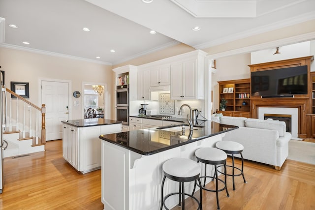 kitchen featuring a sink, a kitchen island, white cabinets, light wood-type flooring, and dark countertops