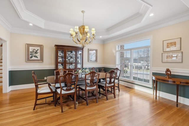 dining room with a raised ceiling, ornamental molding, a notable chandelier, and light wood-type flooring