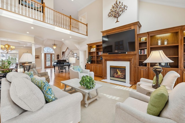 living room with a chandelier, light wood-type flooring, ornamental molding, a towering ceiling, and decorative columns