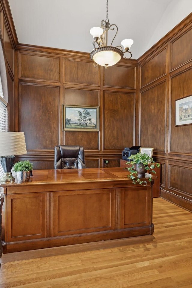 office area with light wood-type flooring, an inviting chandelier, wooden walls, and a decorative wall