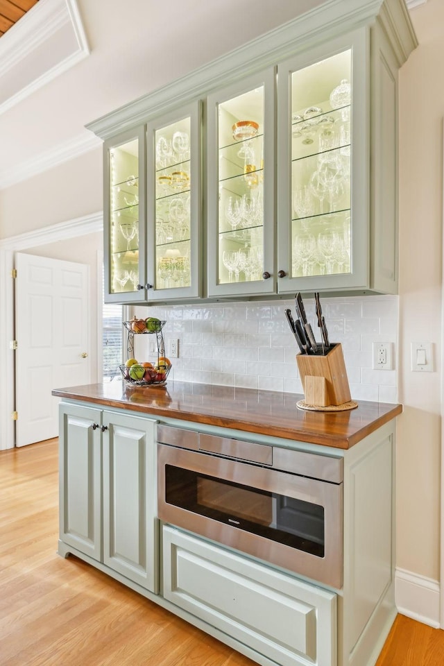 bar featuring tasteful backsplash, stainless steel microwave, ornamental molding, and light hardwood / wood-style floors