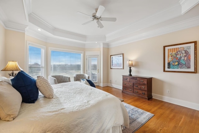 bedroom with baseboards, a raised ceiling, a ceiling fan, wood finished floors, and crown molding