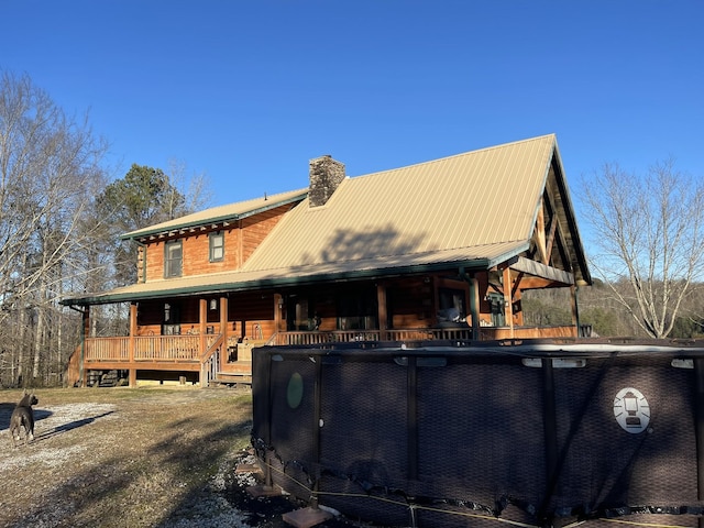 rear view of house with an outdoor pool, covered porch, a chimney, and metal roof