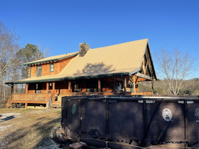 rear view of house featuring a chimney, metal roof, and a porch