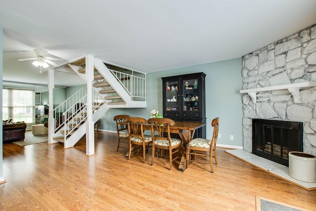 dining space with ceiling fan, a stone fireplace, and hardwood / wood-style floors