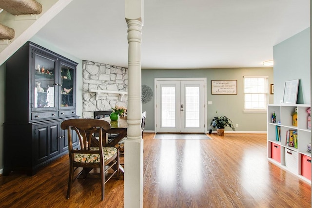 interior space with a stone fireplace, dark hardwood / wood-style floors, ornate columns, and french doors