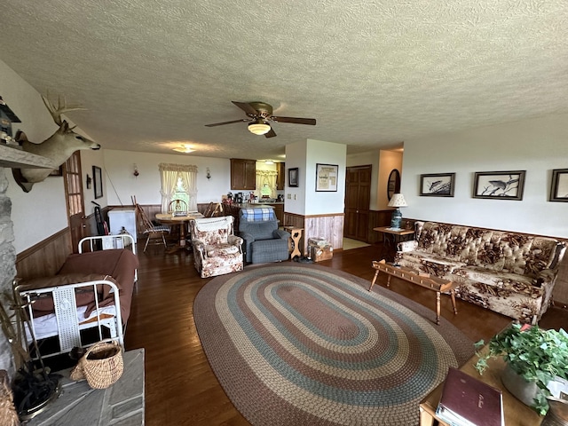 living room featuring ceiling fan, wooden walls, a textured ceiling, and dark hardwood / wood-style flooring