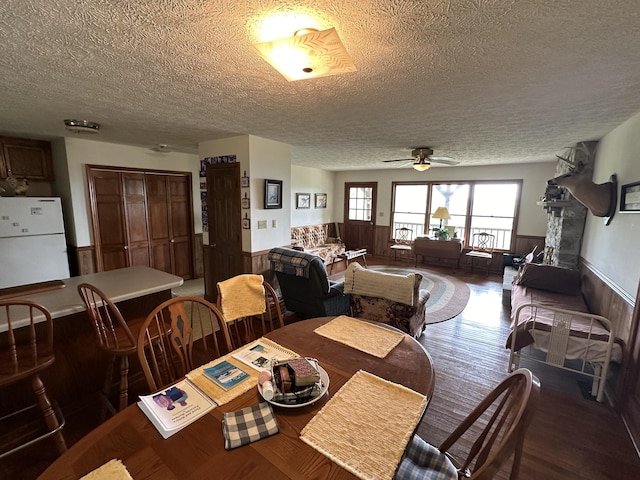 dining area with ceiling fan, dark wood-type flooring, a textured ceiling, and wooden walls