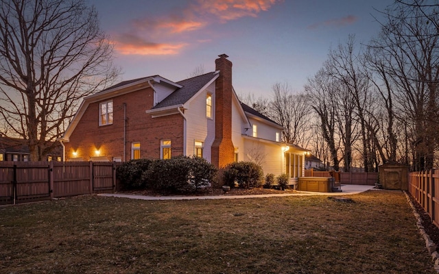 property exterior at dusk with a hot tub, a lawn, and a shed