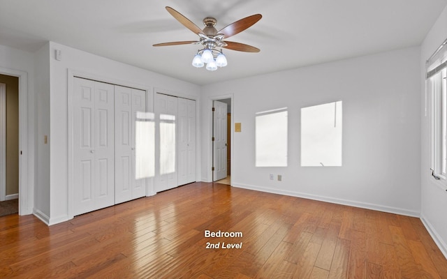 unfurnished bedroom with ceiling fan, light hardwood / wood-style flooring, and two closets