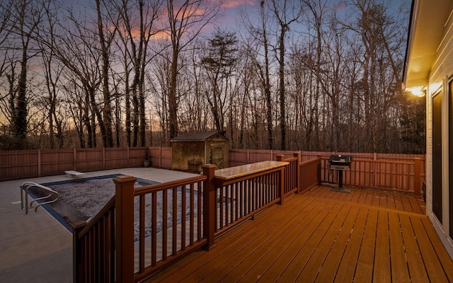 deck at dusk featuring a shed and grilling area