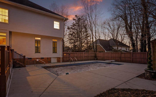 pool at dusk featuring a diving board and a patio