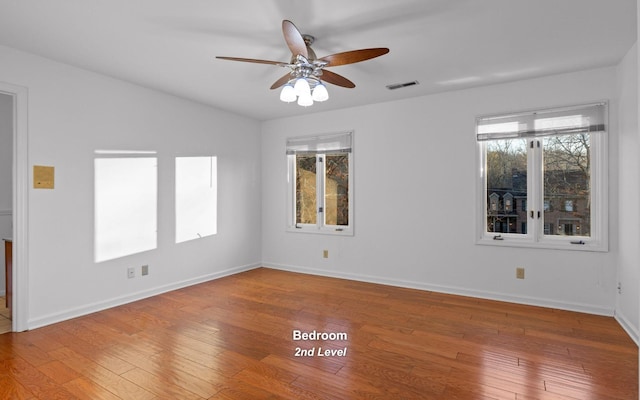 empty room featuring ceiling fan, plenty of natural light, and wood-type flooring