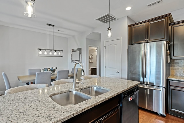 kitchen featuring appliances with stainless steel finishes, hardwood / wood-style floors, sink, hanging light fixtures, and light stone countertops