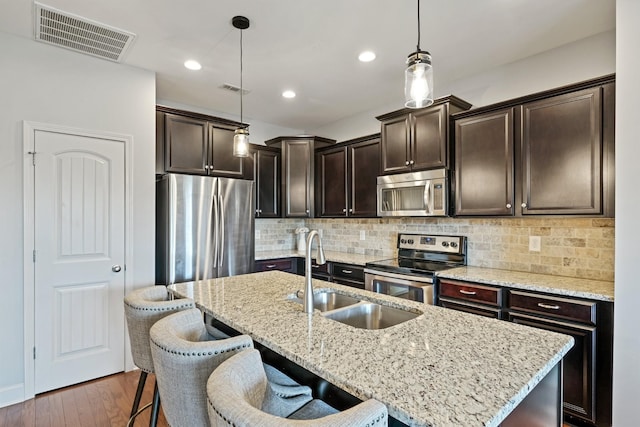 kitchen with sink, light stone counters, decorative light fixtures, a center island with sink, and stainless steel appliances