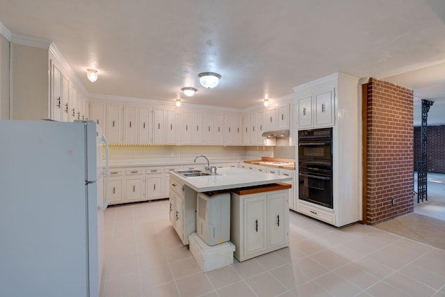 kitchen with double oven, white cabinetry, sink, white fridge, and a center island with sink