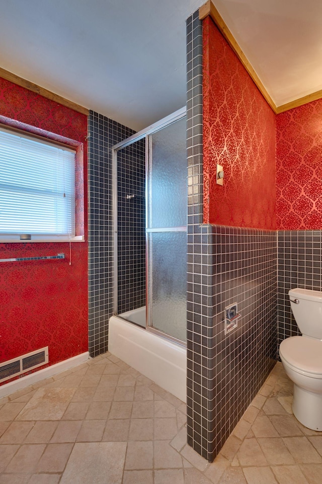 bathroom with tile patterned flooring, enclosed tub / shower combo, tile walls, and toilet