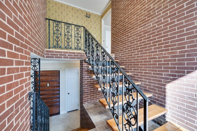 stairs with tile patterned flooring, ornamental molding, brick wall, and a towering ceiling