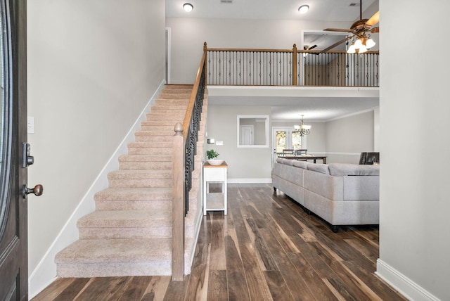 stairs with ceiling fan with notable chandelier, hardwood / wood-style floors, and a high ceiling