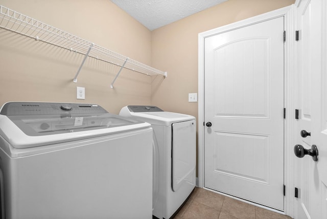 clothes washing area featuring light tile patterned flooring, a textured ceiling, and washer and clothes dryer