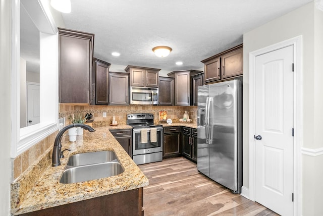 kitchen with sink, appliances with stainless steel finishes, light stone counters, dark brown cabinetry, and decorative backsplash