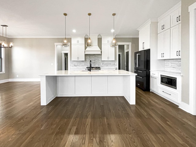 kitchen with high end black refrigerator, built in microwave, hanging light fixtures, custom exhaust hood, and a kitchen island with sink