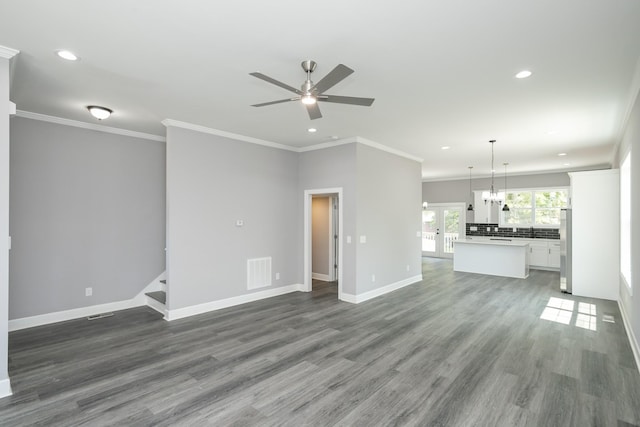 unfurnished living room with crown molding, dark wood-type flooring, ceiling fan with notable chandelier, and french doors