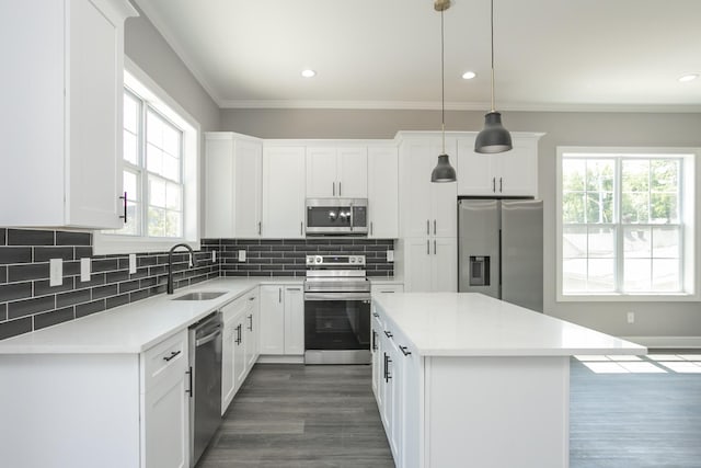 kitchen with sink, hanging light fixtures, stainless steel appliances, white cabinets, and a kitchen island